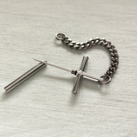 Flat lay of the 304 steel cross toothpick, protective cap, and pure titanium chain on a light fabric surface.