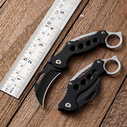 Open and closed Black Bird claw knives beside a metal ruler on wood for size reference.