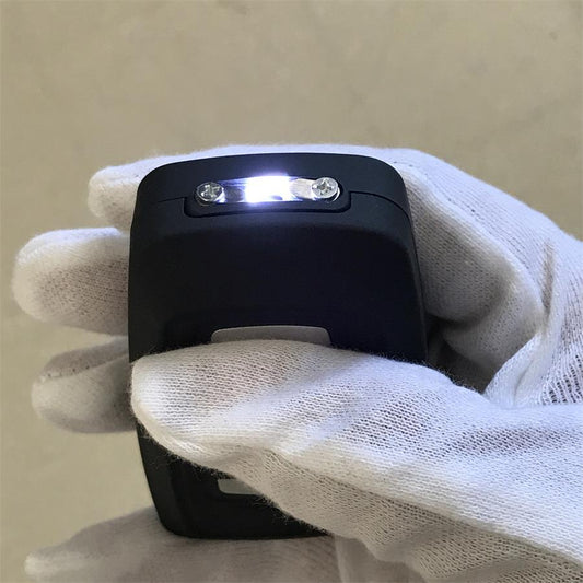 Car key stun gun held in a white-gloved hand with the LED light switched on at the head of the unit