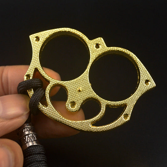 Close-up of the golden sloth finger clasp held between fingers showing the checkered face texture, rivet studs and heart-shaped cutout