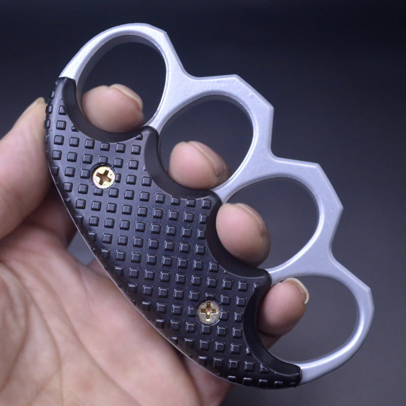 Hand holding the silver gray and black knuckle duster with fingers through the four oval holes for scale on a dark background