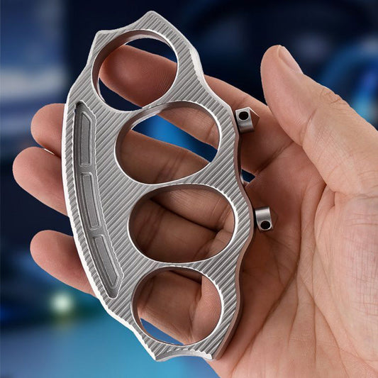 Knuckle duster held in palm showing four finger holes and diagonal machined texture