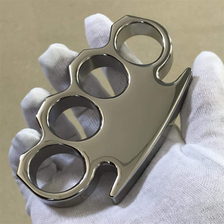 Gloved hand holding the steel knuckle duster from the palm side, pointed tip and lower edge in frame