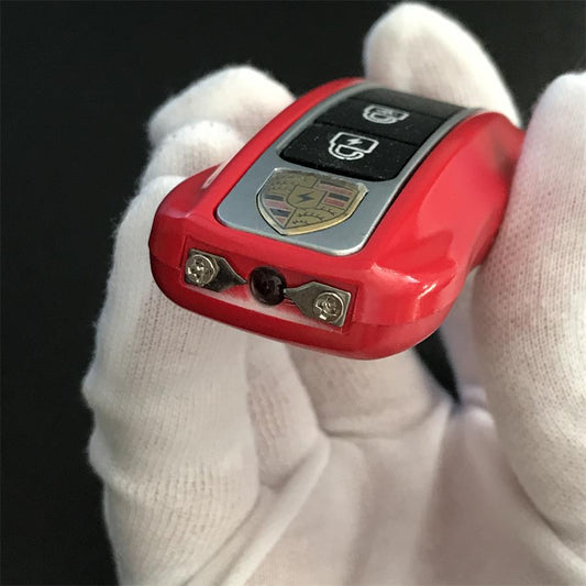 Red car-key style unit held in a white gloved hand showing the twin metal contact pins and central LED lens on the head edge