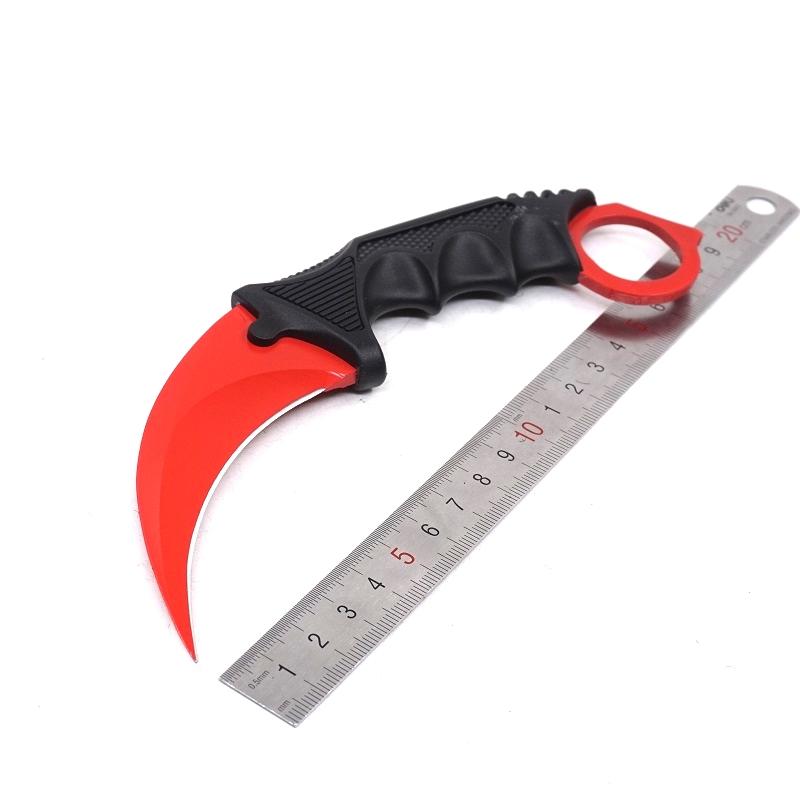 Single red one-hole karambit knife displayed next to a metal ruler