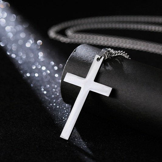 Polished silver cross pendant necklace leaning against black textured cylinder with bokeh light sparkles