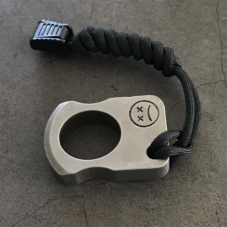 Silver-tone single-hole knuckle weight with black cord lanyard and cord lock on a concrete surface