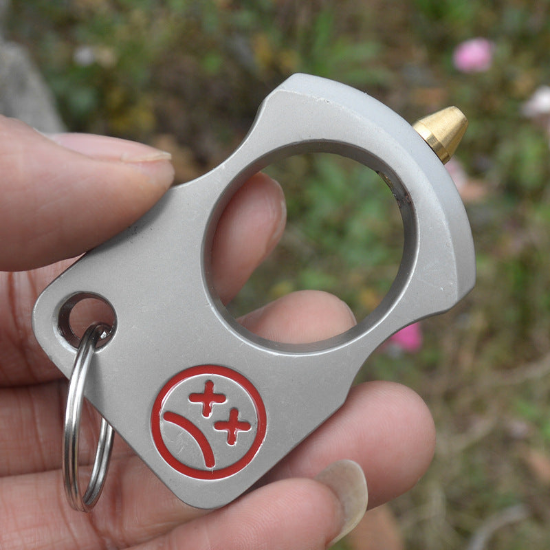 Silver single-hole knuckle keychain held between fingers showing the brass-toned cone tip and red face print