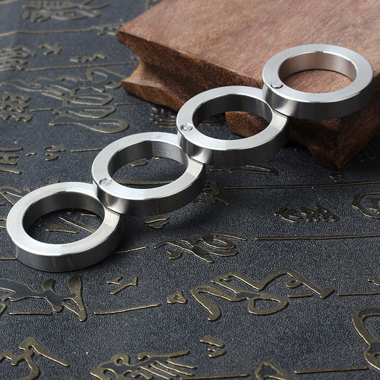 Unfolded four-ring stainless steel row lying diagonally on a dark engraved mat with a wooden block behind, pivot pins visible between the rings