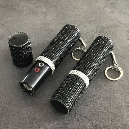 Two black rhinestone mini stun guns with caps removed lying next to decorative cap