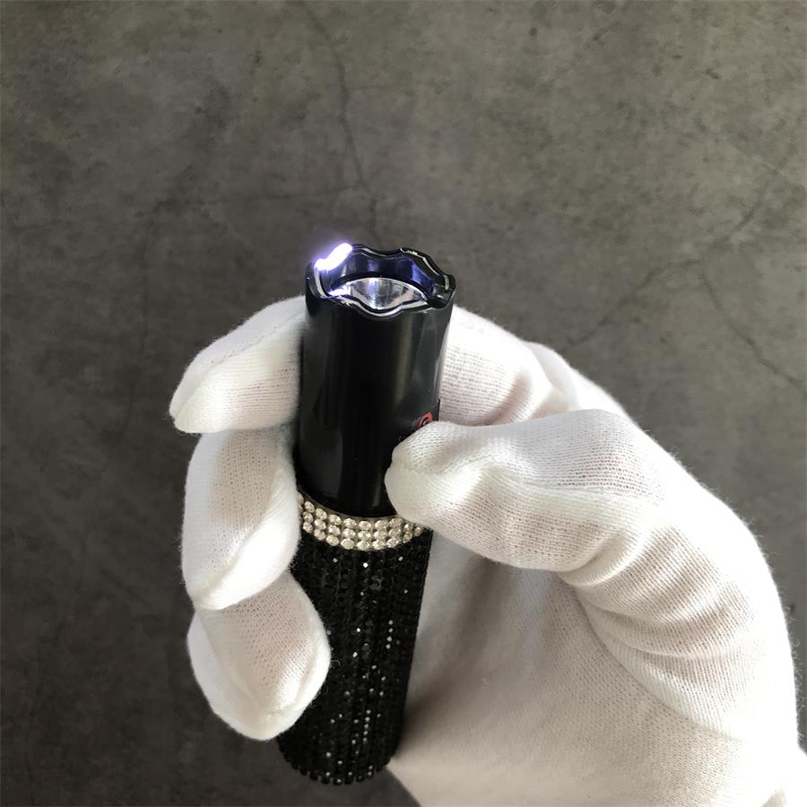 Close-up of black rhinestone mini stun gun with LED flashlight activated in gloved hand