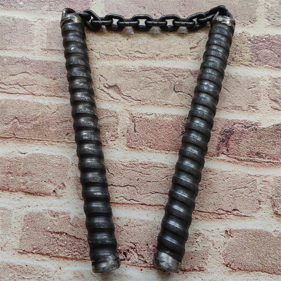 Two black chain baton handles hanging vertically by metal chain on brick-pattern wall