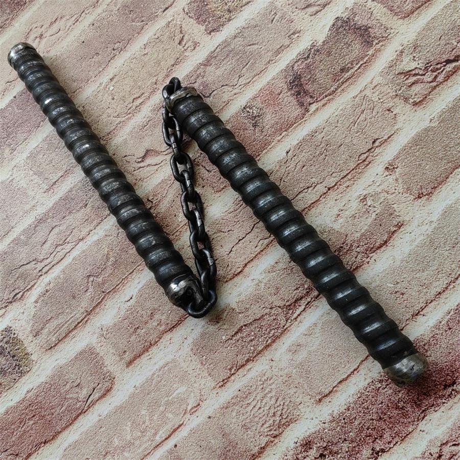 Two black chain baton handles lying side by side connected by metal chain on brick surface
