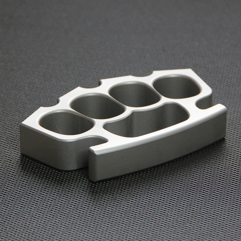 Silver knuckle duster lying flat on black textured surface, palm-side facing up.