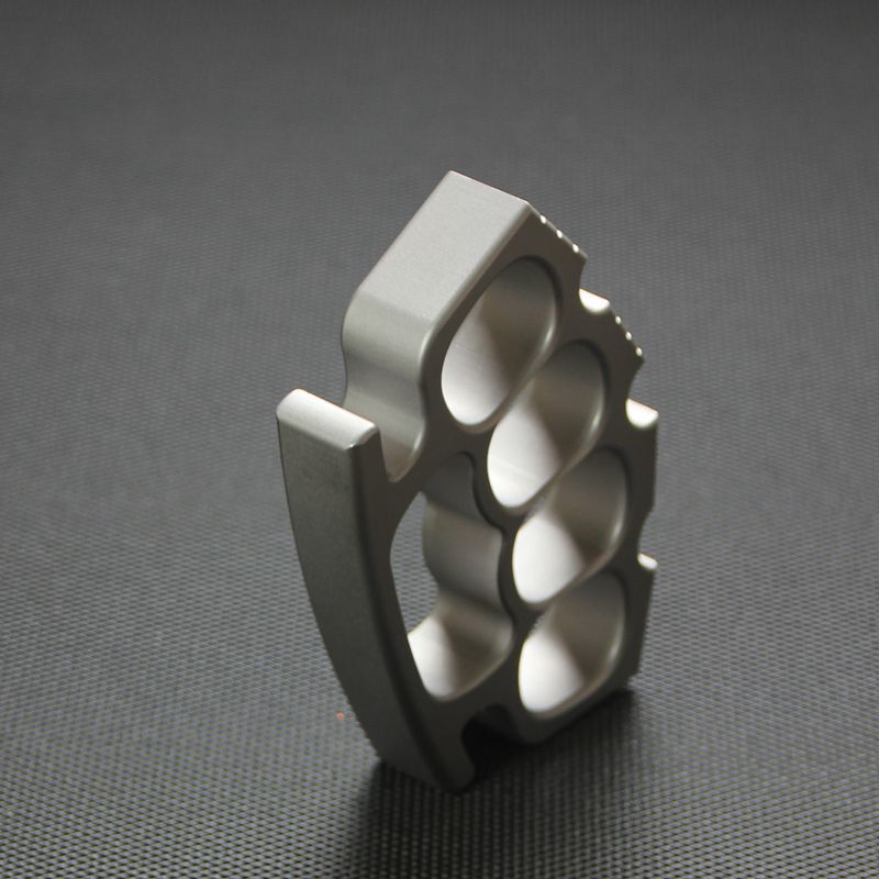 Side profile of silver knuckle duster standing on edge, showing finger holes and thickness.