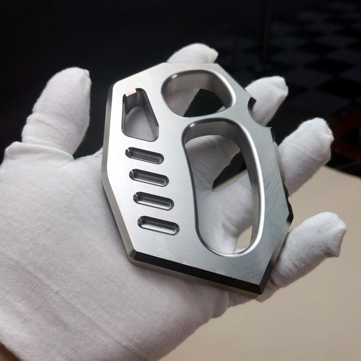 White-gloved hand holding the two-finger rope hole duster from the opposite angle, showing machined slots.