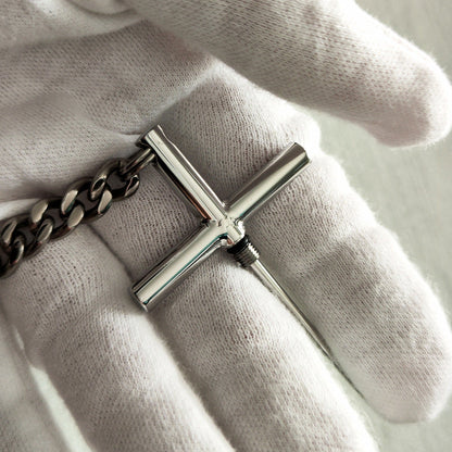 Close-up of the 304 steel cross toothpick with titanium chain in a white-gloved hand.