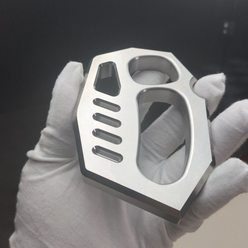 Close-up of the mirror polished two-finger knuckle duster with rope holes and machined slots in a gloved hand.