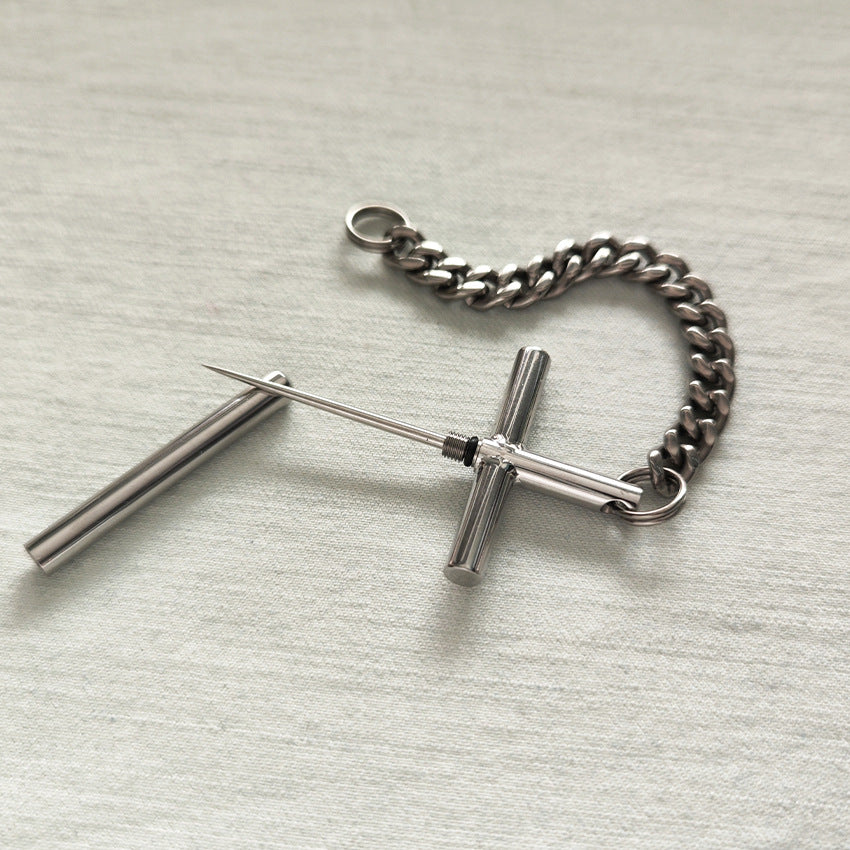 Flat lay of the 304 steel cross toothpick, protective cap, and pure titanium chain on a light fabric surface.