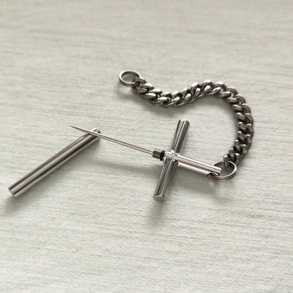 Flat lay of the 304 steel cross toothpick, protective cap, and pure titanium chain on a light fabric surface.
