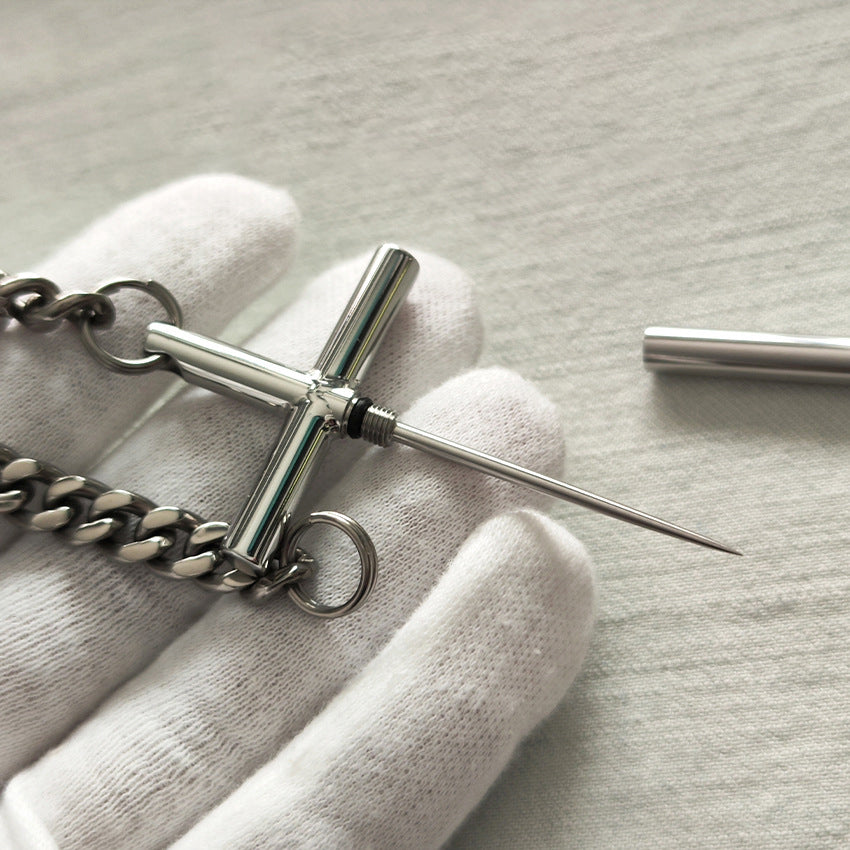 White-gloved hand holding the 304 steel cross toothpick with titanium chain, removable tip extended.