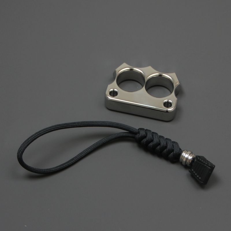 316 steel two-hole mini duster placed next to its black paracord lanyard on a grey surface.