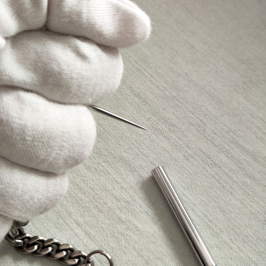 White-gloved hand holding the removable pointed tip next to the protective cap and titanium chain.