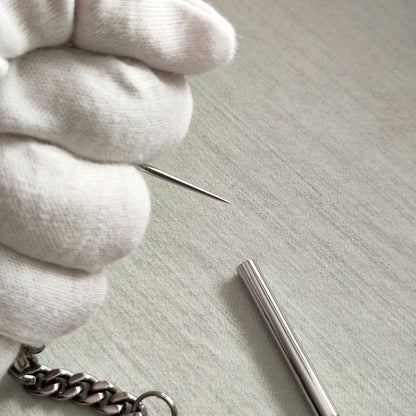 White-gloved hand holding the removable pointed tip next to the protective cap and titanium chain.