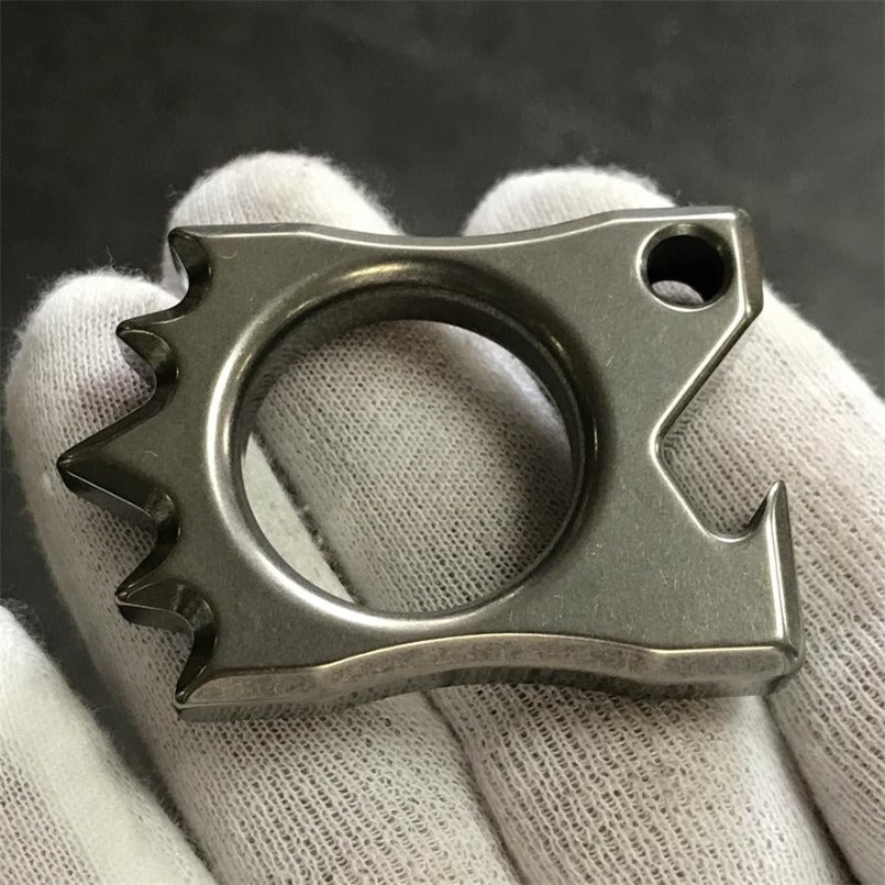 Gloved hand pinching Titanium Knuckle Duster on backdrop