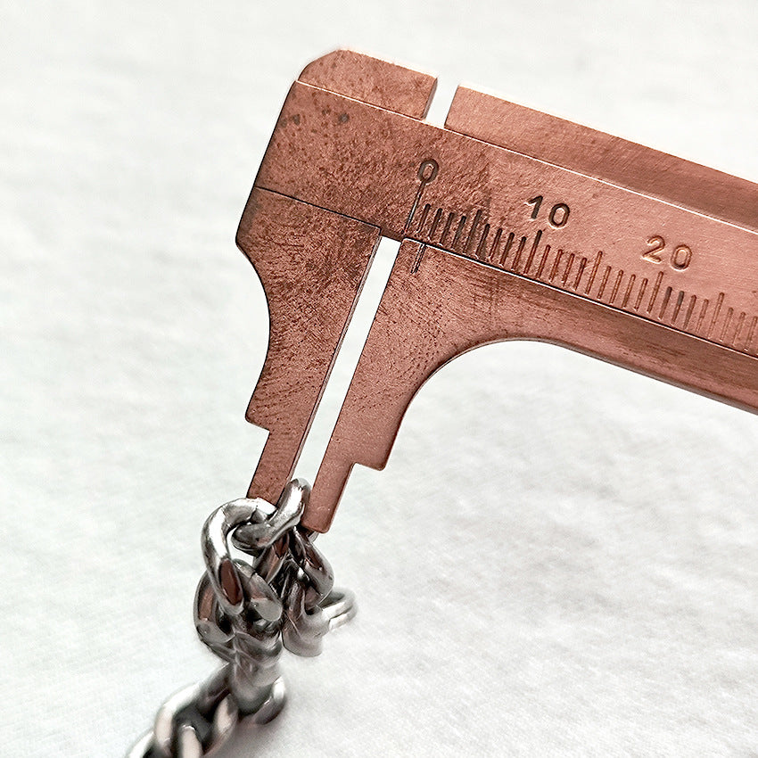 Close-up of the pure titanium chain link thickness being measured with a copper caliper.