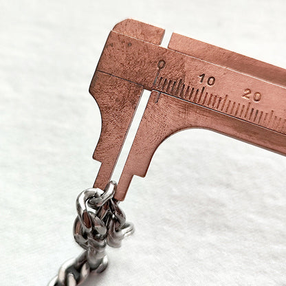 Close-up of the pure titanium chain link thickness being measured with a copper caliper.