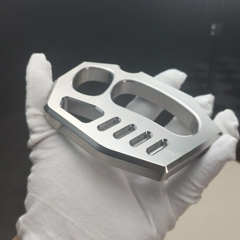 Mirror polished 304 stainless steel two-finger rope hole knuckle duster held in a white-gloved hand, angled view.