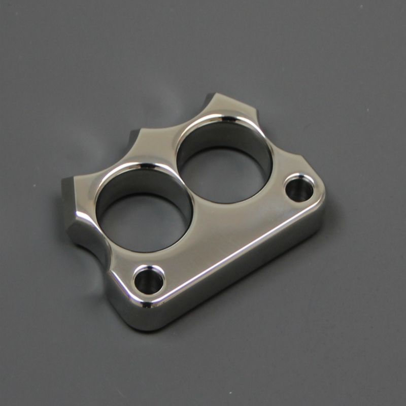 Mirror polished 316 stainless steel two-hole mini knuckle duster lying on a dark grey surface, top view.