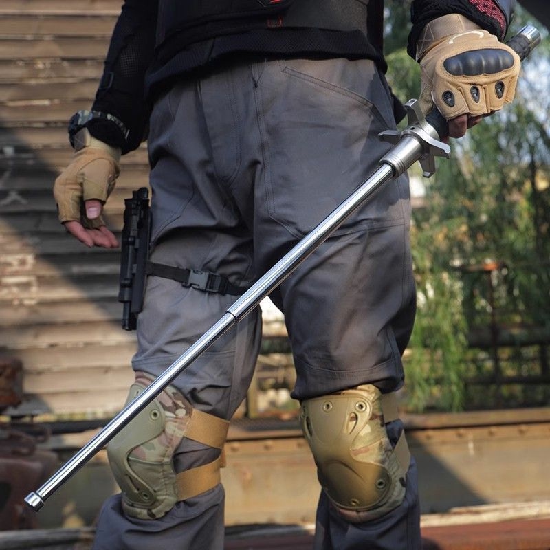 Person in tactical gear holding an extended aviation alloy steel baton outdoors
