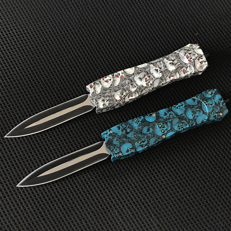 Two OTF pocket knives with white skull and blue floral handles side by side
