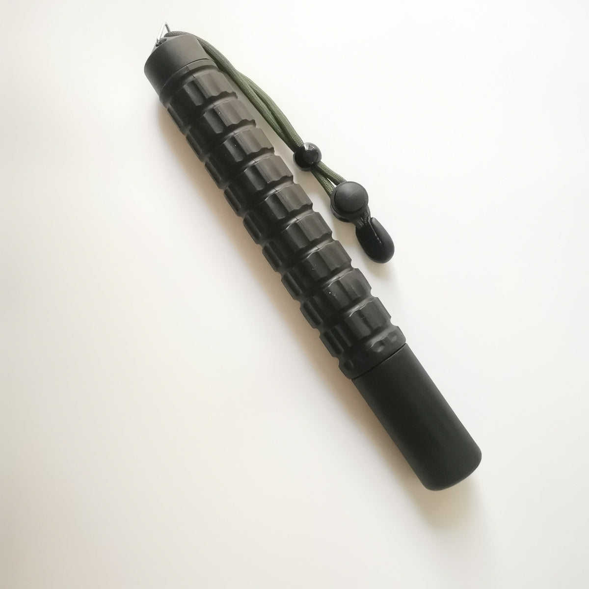 Collapsed black baton on a white background with the green cord hanging beside
