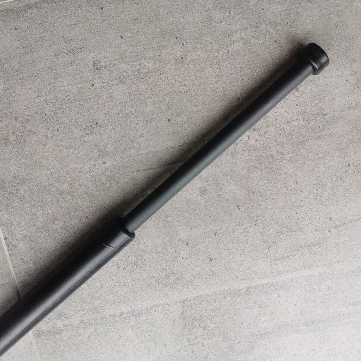 Black baton extended diagonally across a concrete floor with the thin shaft out