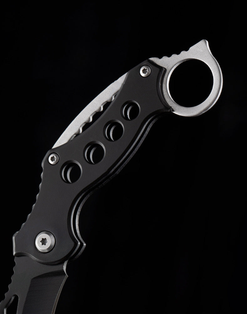 Close-up of the black handle and finger ring on the folding EDC claw knife against a black background.