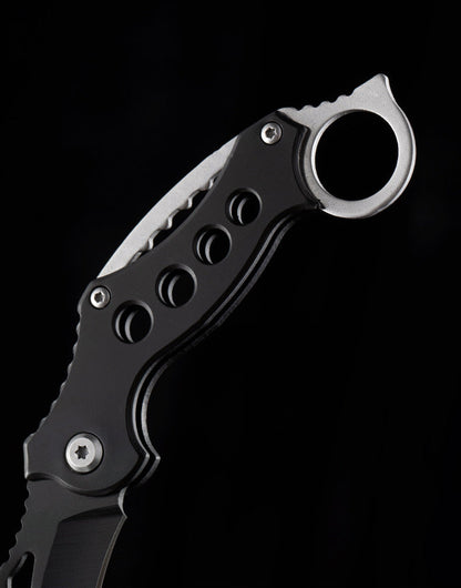 Close-up of the black handle and finger ring on the folding EDC claw knife against a black background.