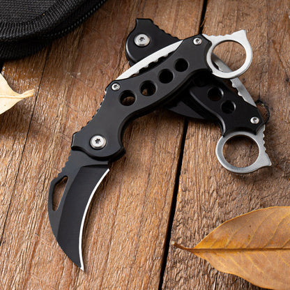 Two Black Bird folding claw knives crossed on wood, one open and one closed, with dry leaves.