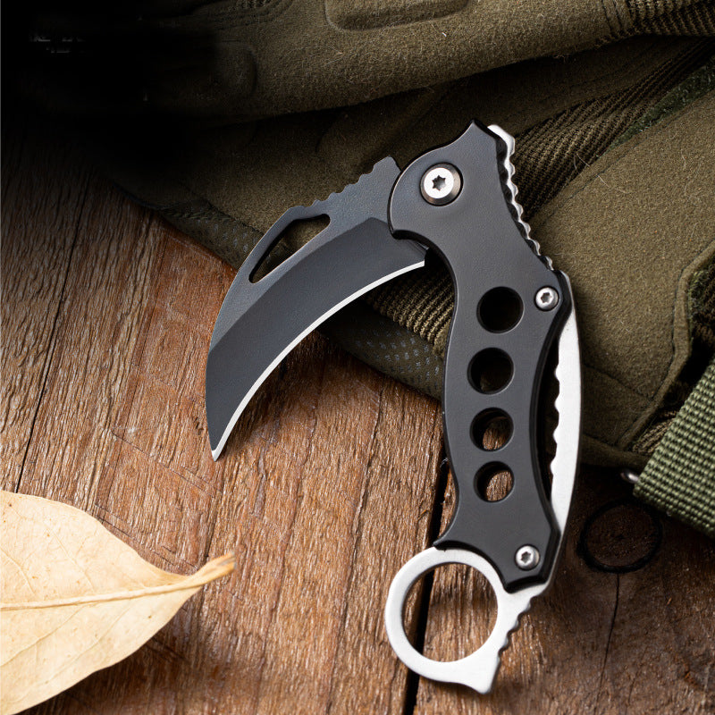 Open Black Bird folding claw knife placed on a green tactical bag with a dry leaf nearby.