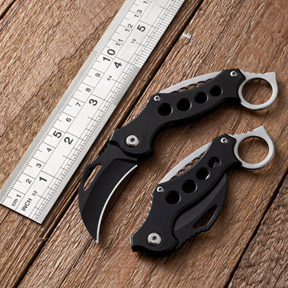 Open and closed Black Bird claw knives beside a metal ruler on wood for size reference.