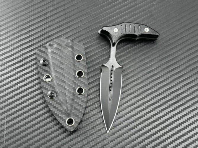 Black blade push dagger next to its carbon fiber sheath on textured background