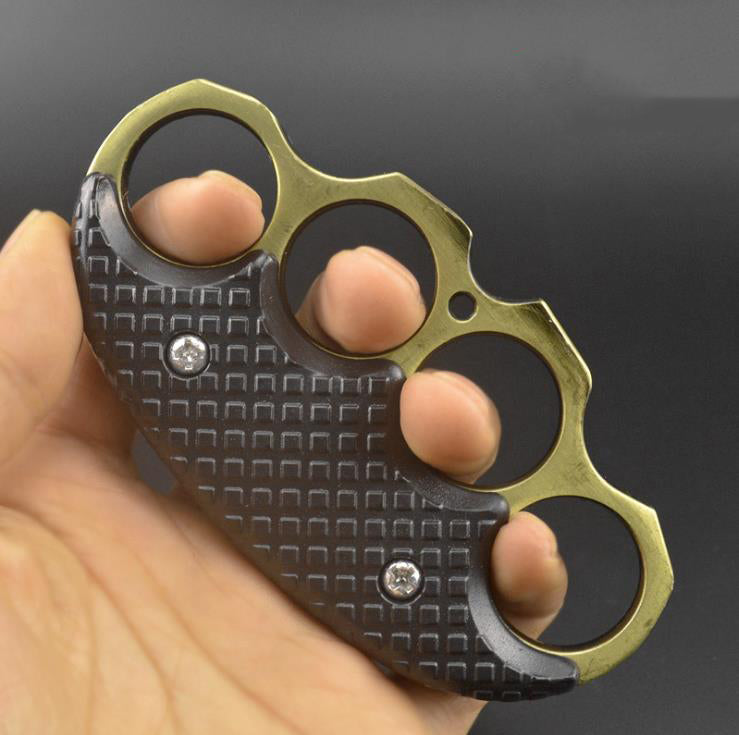 Brass-gold ring black-covered knuckle duster held in a hand, side angle view.