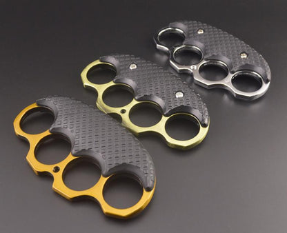 Five black-covered EDC knuckle dusters in Gold, Silver, Bronze, Black and Rose Gold laid on a dark surface.