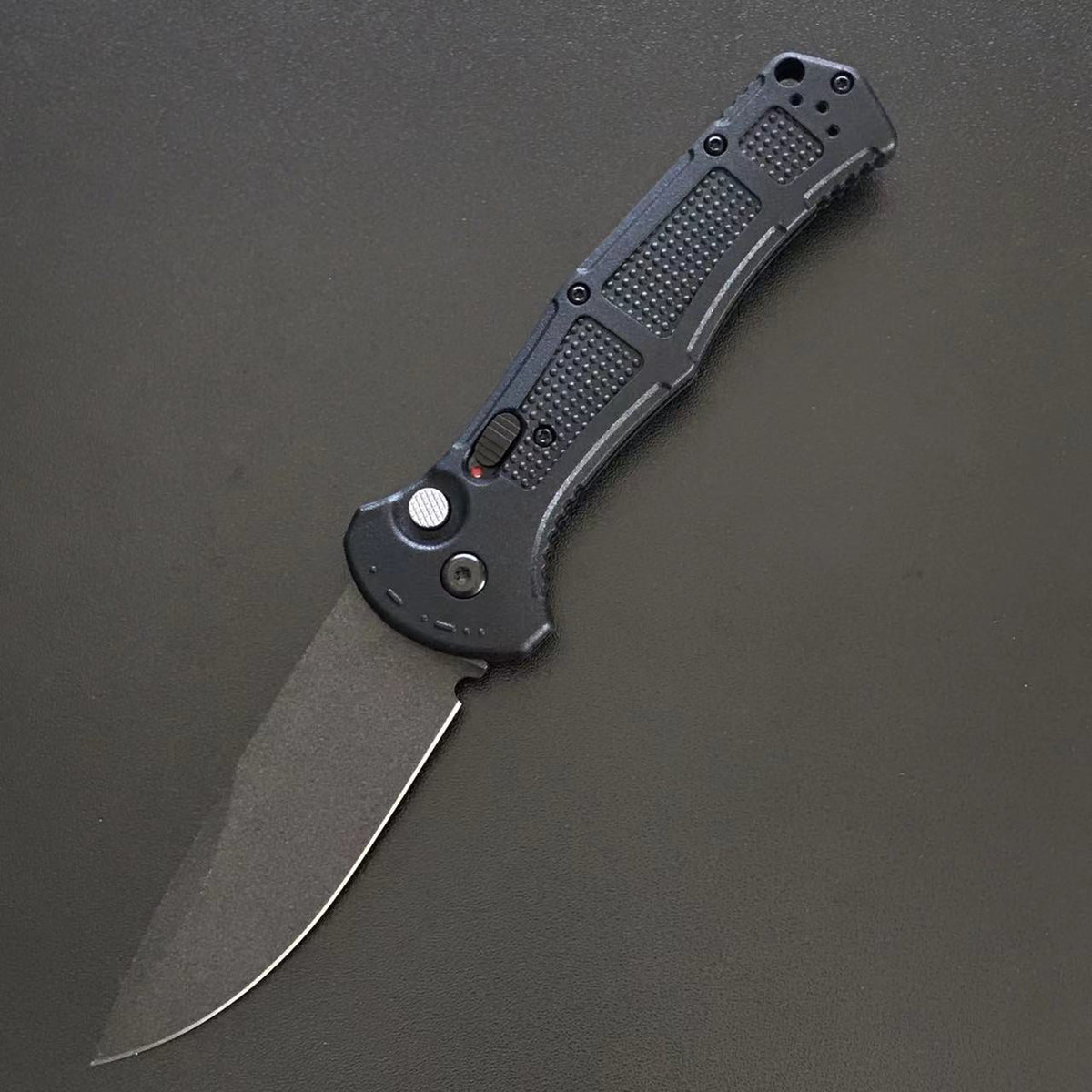 Black handle folder open with a plain drop-point blade on a grey surface