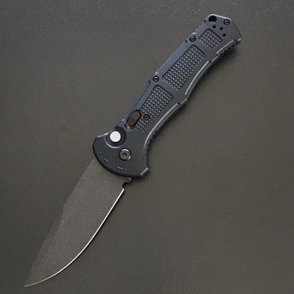 Black handle folder open with a plain drop-point blade on a grey surface