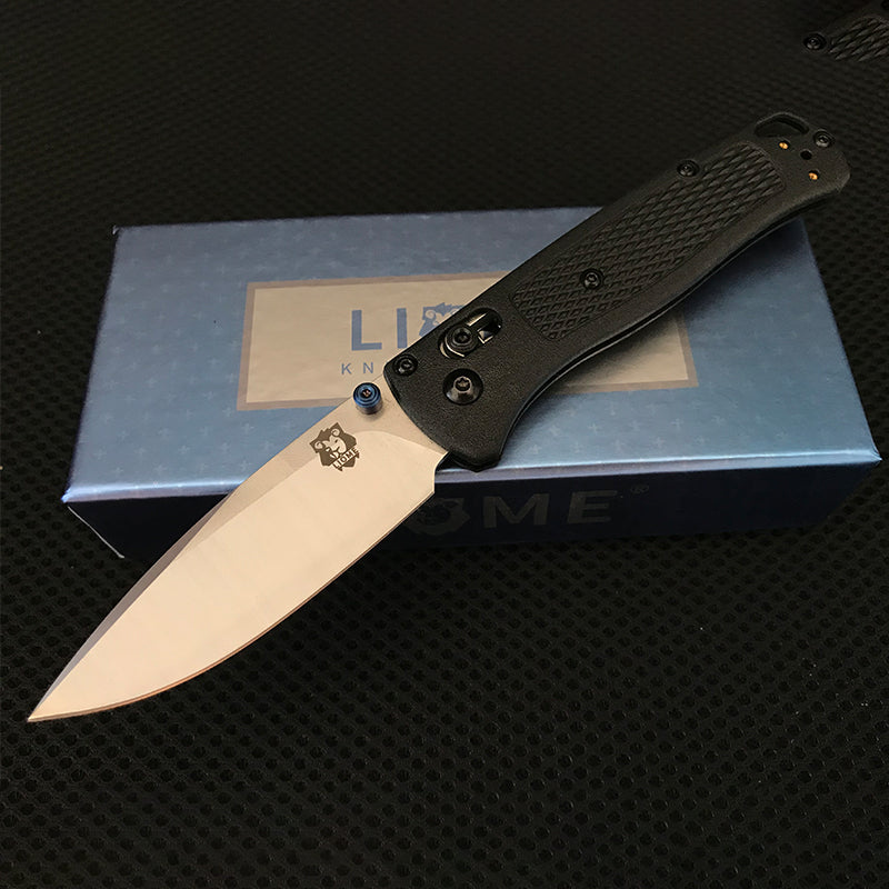 Black handled folding knife with polished silver drop-point blade open across a Liome branded box