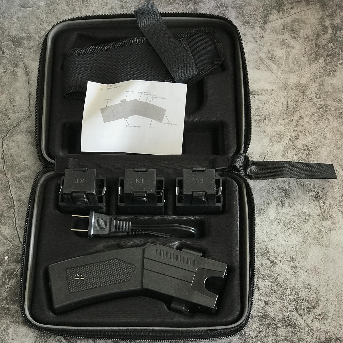 Black zippered hard case laid open showing the black stun gun unit, three KT launcher cartridges, wall charger cable, nylon holster and the printed user manual diagram