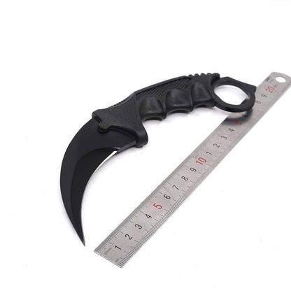 Single black one-hole karambit knife displayed next to a metal ruler